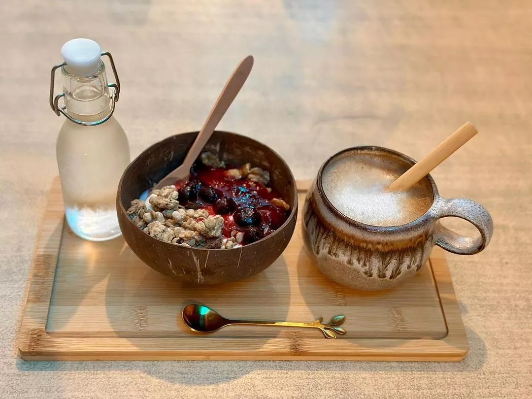 Botella de agua, bol con frutos secos y frutos rojos y un café sobre una bandeja de madera